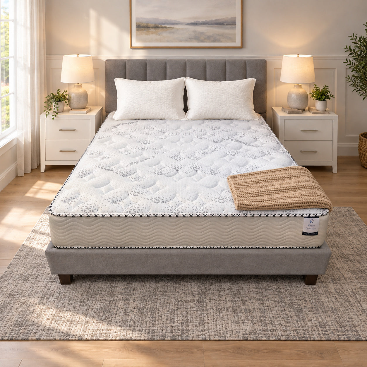 Olympic Queen Breeze Cool Max 10" Medium Firm Tight top mattress on a gray upholstered bed with two white pillows and a tan knit throw, in a bedroom with white nightstands, table lamps and a framed landscape print